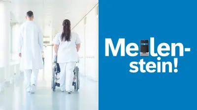 Ein Krankenhausflur, in dem von hinten ein Mann und eine Frau in weißer Arbeitskleidung zu sehen sind. Die Frau schiebt einen Rollstuhl.