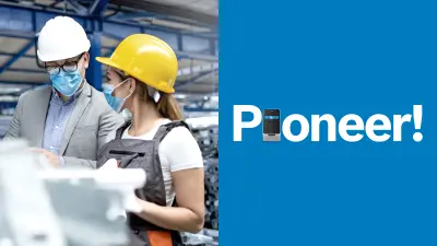 A warehouse with lots of pallets. A man and a woman are talking. Both are wearing blue surgical masks and helmets. The man is wearing a shirt and jacket, the woman, a white t-shirt and dungarees.