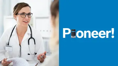 A doctor is sitting at a table and talking to a woman who can be seen from behind, slightly blurred. The doctor has a clipboard with sheets of paper in front of her.